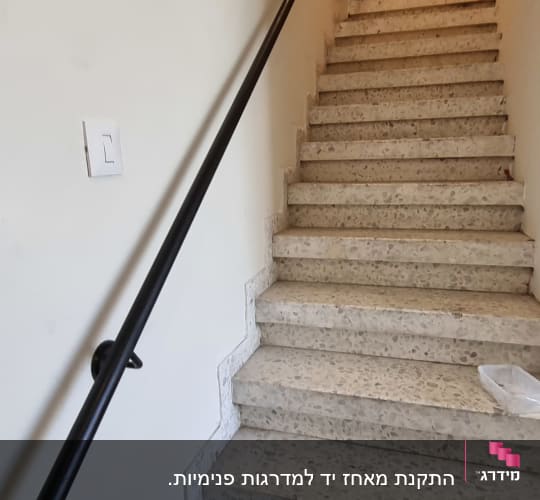 מעקה ממתכת שחור מותקן על הקיר לאורך גרם מדרגות